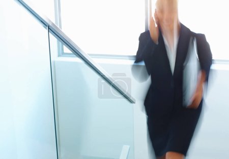 Foto de Mujer con portátil usando teléfono celular. Movimiento borroso de la mujer de negocios con el ordenador portátil usando el teléfono celular al subir las escaleras - Imagen libre de derechos
