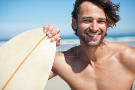 Téléchargez les photos : Sourires d'été. Un jeune homme attrayant tenant sa planche de surf sur la plage - en image libre de droit