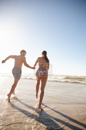 Photo for Race you. Rearview shot of a young couple running into the sea together - Royalty Free Image