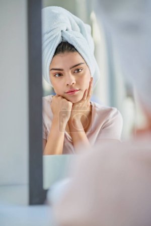 Foto de ¿Debo ir natural hoy... una hermosa mujer joven preparándose en el espejo del baño en casa - Imagen libre de derechos
