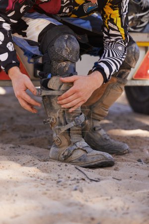 Photo for Prepping before the race. a dirt bike rider putting on his protective boots - Royalty Free Image