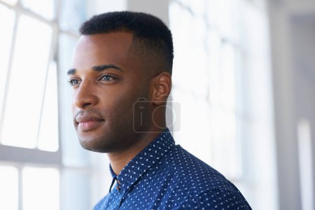 Photo for Contemplating his future. Profile of a young ethnic man looking thoughtfully out of a window - Royalty Free Image