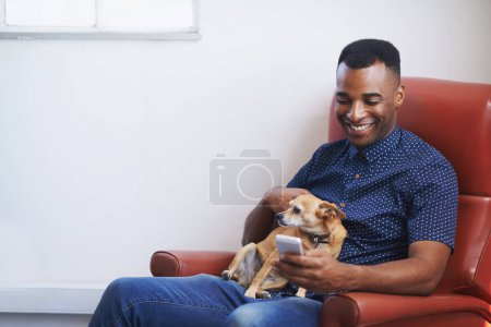 Foto de Comunicación y compañerismo. Un joven guapo usando su celular con su perro en su regazo - Imagen libre de derechos