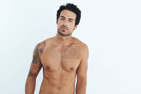 Portrait, body and muscle with a sexy man in studio on a white background for masculine desire. Shirtless, tattoo and manly with a handsome young male model posing topless for rugged sensuality.