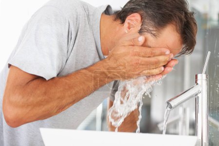Téléchargez les photos : Hygiène, hydratation et un homme se lave le visage dans la salle de bain de sa maison le matin pour se réveiller. Frais, l'eau et le nettoyage avec un homme dans sa maison pour commencer une routine de soins de la peau ou de l'humidité. - en image libre de droit
