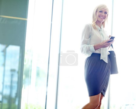 Téléchargez les photos : Communication en déplacement. femme d'affaires souriante entrant dans le bureau en regardant son téléphone portable avec copyspace - en image libre de droit