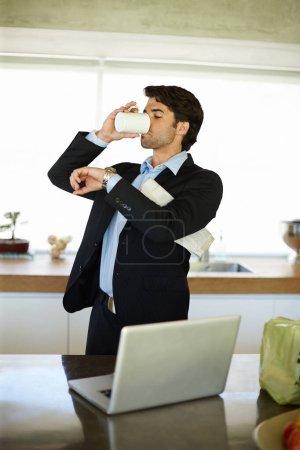 Téléchargez les photos : Je vérifie son temps. un homme d'affaires pressé buvant du café et utilisant son ordinateur portable dans sa cuisine - en image libre de droit