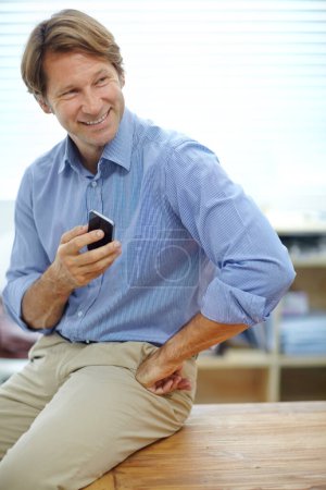 Photo for Business communication. a mature businessman sending a text while leaning on a table in his office - Royalty Free Image