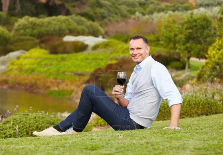Foto de Hombre maduro con vino tinto al aire libre, relajarse con sonrisa en la naturaleza con bebida alcohólica, ocio y viajes al campo. Hombre feliz con bebida alcohólica en vaso, satisfecho y relajante en el parque. - Imagen libre de derechos