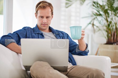 Téléchargez les photos : Prendre le temps de travailler sur son blog. un bel homme prenant un café tout en utilisant son ordinateur portable - en image libre de droit