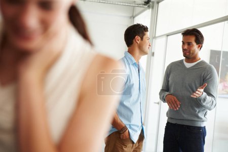 Photo for Office scandal. Two colleagues in the office gossiping about a third colleague standing in the foreground - Royalty Free Image