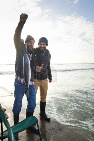 Foto de Mi mayor captura hasta ahora. dos jóvenes pescando en el océano - Imagen libre de derechos