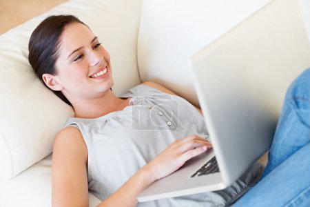 Photo for Relax, happy woman and laptop on a sofa streaming, social media and reading in her home. Lying down, smile and female online in a living room with subscription, entertainment and internet search. - Royalty Free Image