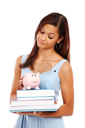 Photo for You need to save in order to study. Young woman holding some textbooks and a piggybank against a white background - Royalty Free Image
