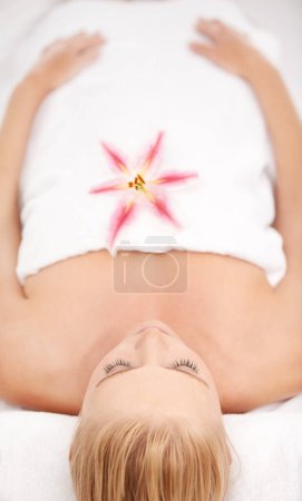 Photo for Natural beauty retreat. A young woman relaxing at a spa with a tiger lily lying on her chest - Royalty Free Image