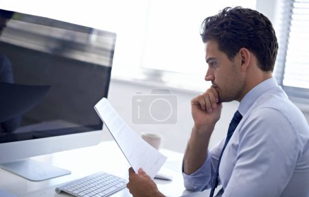 Foto de Leyendo la letra pequeña. Un joven empresario revisando un contrato mientras está sentado en su puesto de trabajo - Imagen libre de derechos