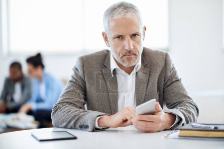 Photo for Serious about his business. a mature businessman using a cellphone while sitting at a table in an office - Royalty Free Image