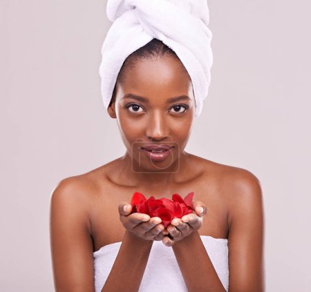 Photo for Skin as soft as rose petals. A studio shot of a beautiful young woman holding red petals and wearing a towel on her head - Royalty Free Image