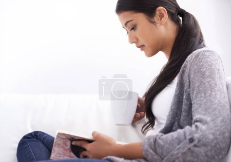 Photo for Reading helps her relax. A pretty young woman relaxing with a book at home - Royalty Free Image