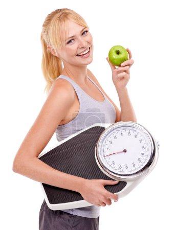 Foto de La pérdida de peso a través de una alimentación saludable. Una mujer sosteniendo una balanza y comiendo una manzana - Imagen libre de derechos