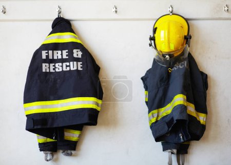 Firefighter, uniform and clothing hanging on wall rack at station for fire fighting protection. Fireman gear, rescue jacket and helmet with reflector for emergency services, equipment or department.