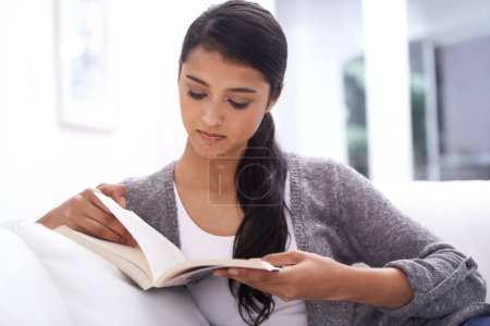 Photo for Shes absorbed...A beautiful young woman reading a book at home - Royalty Free Image