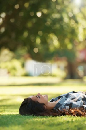 Téléchargez les photos : Relaxant i. Jeune femme allongée sur le dos sur l'herbe dans un parc - en image libre de droit