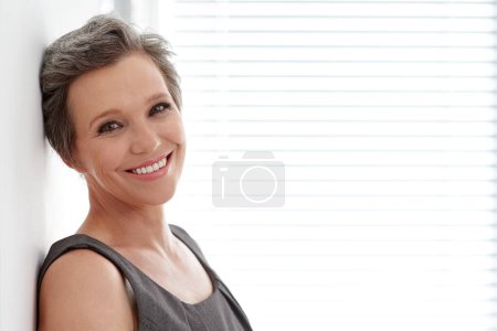 Téléchargez les photos : Satisfaction professionnelle complète. Portrait d'une femme d'affaires mature appuyée contre un mur dans son bureau - en image libre de droit