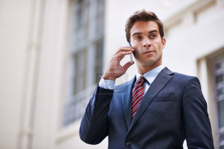 Foto de Comunicaciones urbanas. Un hombre de negocios guapo con un traje hablando en su teléfono móvil en un entorno de ciudad - Imagen libre de derechos