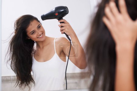 Putting together her hairstyle. A young woman blowdrying her hair