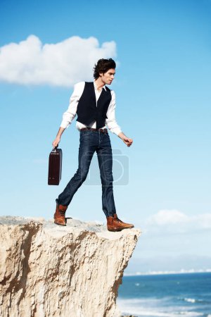 Foto de Práctica de negocios sin miedo. Hombre de negocios semi-formal guapo caminando hacia el borde de un acantilado con vistas al océano - Imagen libre de derechos