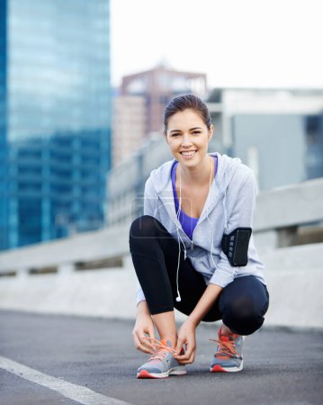Téléchargez les photos : Ça va m'aider à courir plus vite. Portrait d'une jeune joggeuse attachant ses chaussures avant une course à travers la ville - en image libre de droit