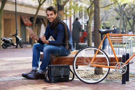 Téléchargez les photos : Connexion dans la ville. un homme utilisant sa tablette tout en faisant une pause dans la ville avec son vélo à côté de lui - en image libre de droit