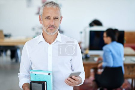 Photo for On my way home. Portrait of a mature businessman using a cellphone while standing in an office - Royalty Free Image