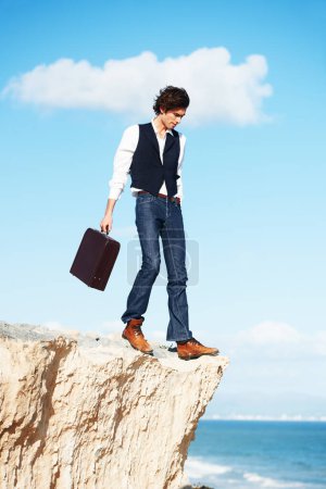 Foto de Viviendo al límite. Joven hombre de negocios semi-formal caminando hacia el borde de un acantilado con vistas al océano - Imagen libre de derechos