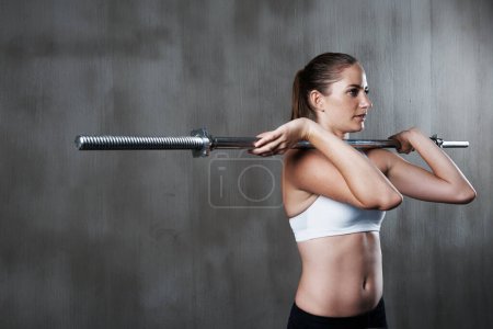 Photo for Fitness, exercise and woman with barbell at gym for bodybuilding, strength or endurance on wall background. Weightlifting, training and female with strong mindset at sports center for intense workout. - Royalty Free Image