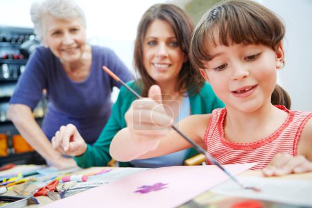 Photo for Creativity is seeing things that others cant. a little girl painting pictures with her mother and grandmother in the background - Royalty Free Image