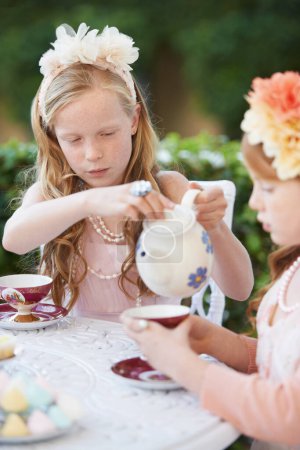Téléchargez les photos : Je peux vous en verser plus ? Deux jeunes filles faisant une partie de thé dans le jardin - en image libre de droit
