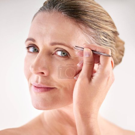 Photo for Tending to her eyebrows. Cropped portrait of a mature woman plucking her eyebrows with a pair of tweezers - Royalty Free Image
