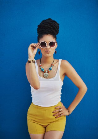 Téléchargez les photos : Face au monde avec son look le plus drôle. une jolie jeune femme portant des lunettes de soleil funky sur un fond bleu - en image libre de droit