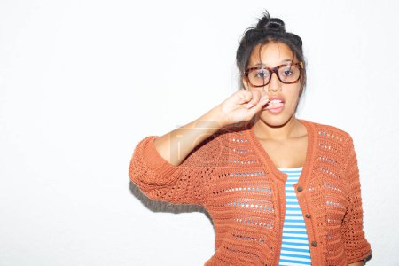 Foto de Hipster chic. Joven mujer hipster mordiéndose el dedo mientras está de pie contra una pared blanca - Imagen libre de derechos