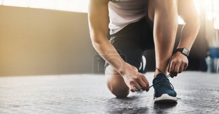 Photo for Sports, athlete and man tie shoes in a gym before workout for health, wellness and endurance training. Fitness, sneakers and closeup of male person tying laces to start a exercise in sport center - Royalty Free Image
