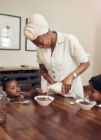 Téléchargez les photos : Le petit déjeuner est le repas le plus important de la journée. une jeune mère préparant des céréales pour ses deux adorables jeunes filles à la maison - en image libre de droit