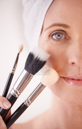 Foto de Herramientas para la belleza. Retrato recortado de una mujer madura sosteniendo pinceles de maquillaje junto a su cara - Imagen libre de derechos