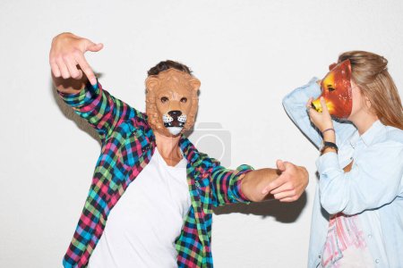 Téléchargez les photos : Embrasser leur côté sauvage. Jeune hipster portant un masque de lion et gesticulant aux côtés d'une jeune femme portant un masque d'ours - en image libre de droit