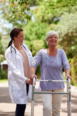 Téléchargez les photos : Avancer tous les jours. Plan extérieur d'un médecin aidant une femme âgée à marcher avec un marcheur orthopédique - en image libre de droit
