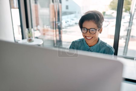 Téléchargez les photos : Tout mon dur labeur commence à porter ses fruits. une jeune femme d'affaires séduisante assise seule et travaillant sur son ordinateur au bureau - en image libre de droit