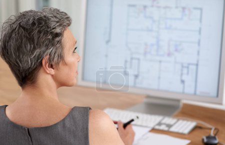 Photo for Genius is 1 talent and 99 hard work. A mature female architect working on building plans on her touchscreen computer - Royalty Free Image