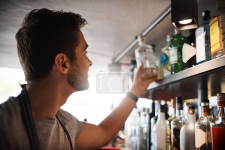 Téléchargez les photos : Il connaît un grand verre quand il en voit un. un jeune homme regardant la marchandise sur les étagères derrière un comptoir de bar - en image libre de droit