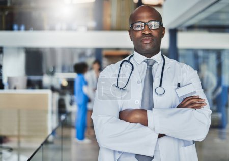 Téléchargez les photos : Votre santé passe avant tout. Portrait d'un médecin confiant travaillant dans un hôpital avec ses collègues en arrière-plan - en image libre de droit